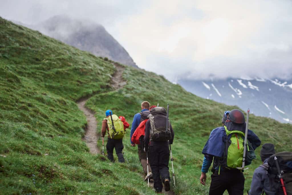 hikers walking up grassy mountain trail 2026 09 23 02 54 10 utc